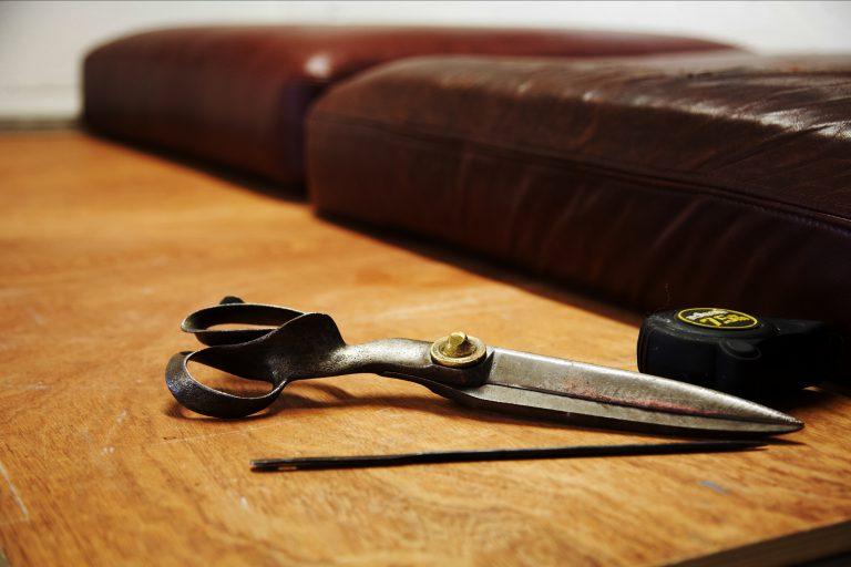 Close up of fabric scissors and tape on table with cushions