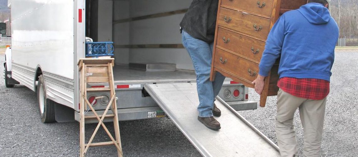 two men carry chest of drawers onto a moving van